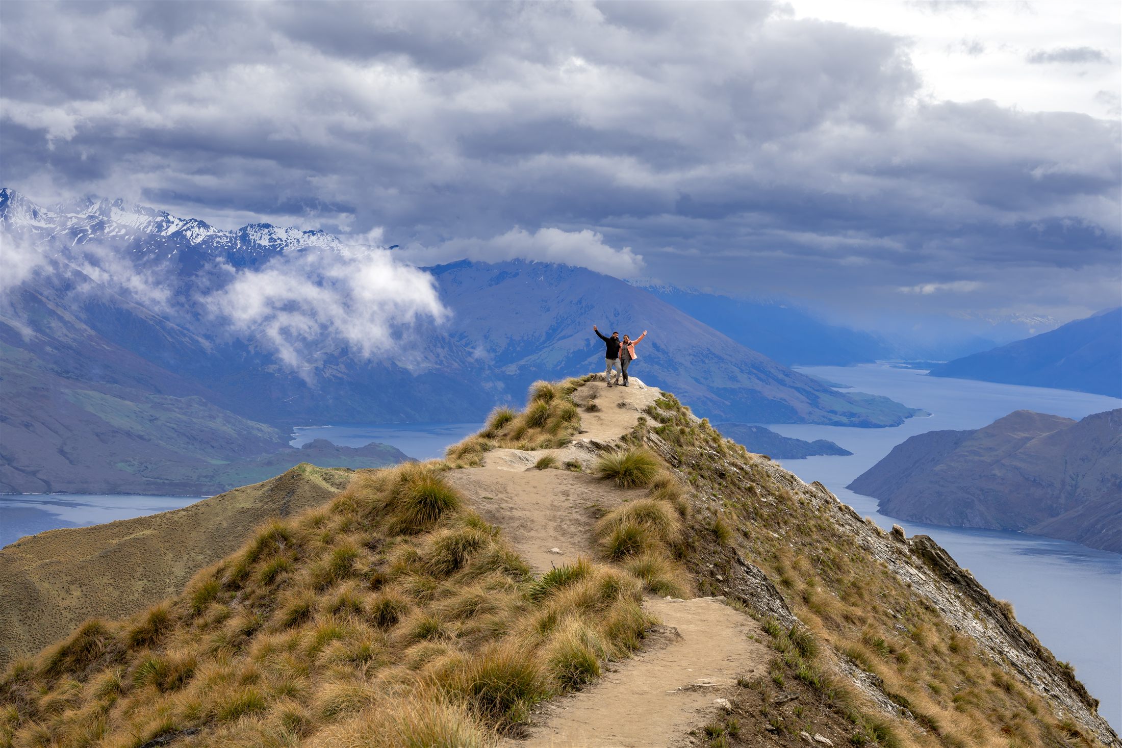 Hiker standing on a mountain ridgeline above a lake, New Zealand