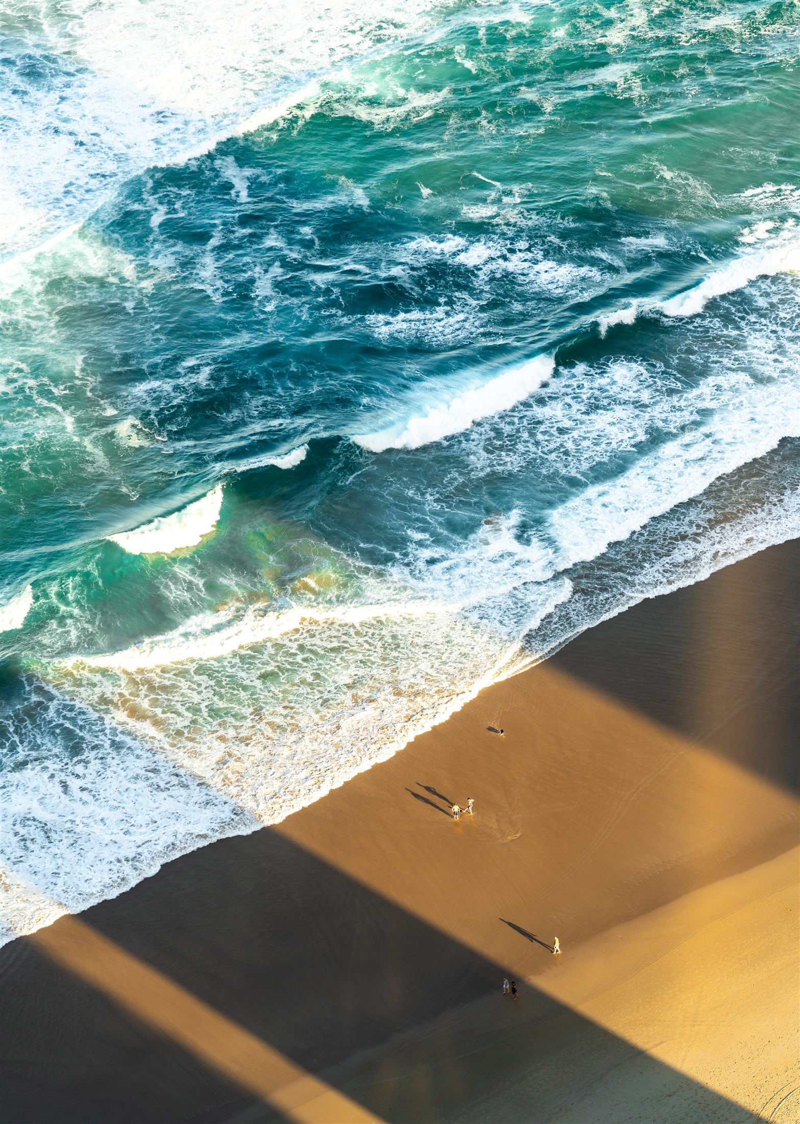 Aerial view of a turquoise wave breaking on golden sand